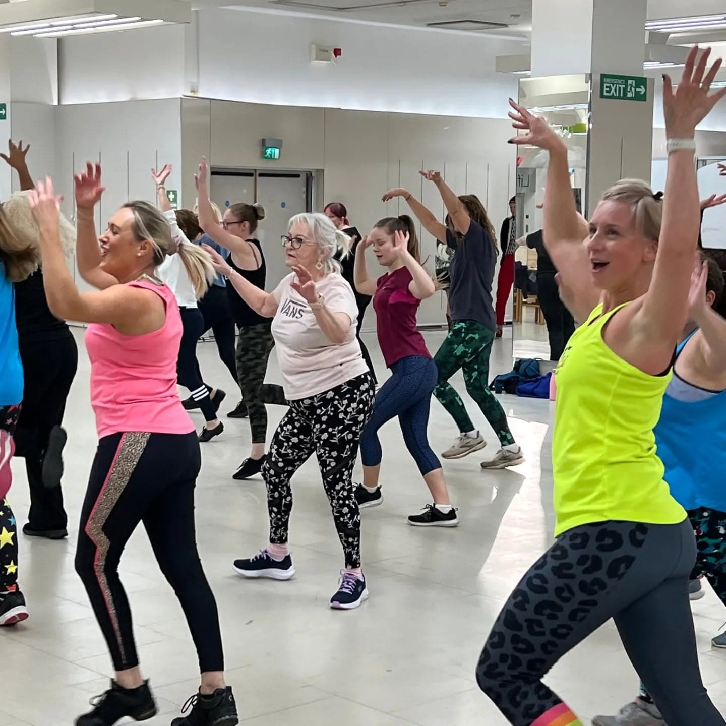 Deelnemers dansen lachend met opgeheven armen tijdens een ChiChi Fit les — plezier en groepsdynamiek